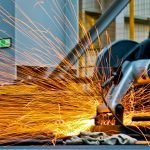 A worker operates a grinder cutting metal, creating a vibrant display of sparks in an industrial setting.